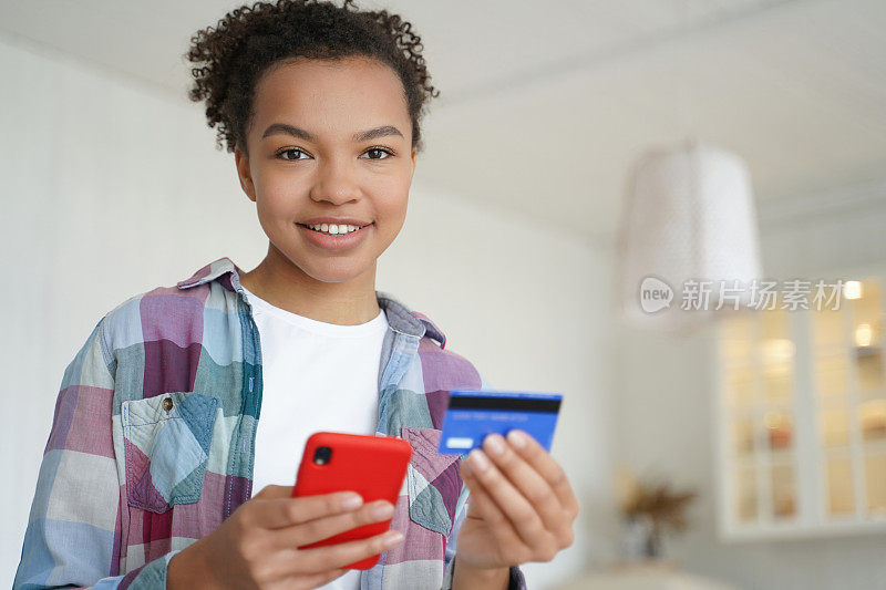 Happy biracial teen pays with credit card, smartphone. Using online banking, e-bank apps. Secure purchase, money transfer at home.